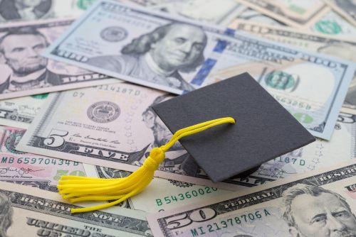 Graduation cap university or college degree on US dollars banknotes background. Visual concept for legal blog discussing discharging student loans in bankruptcy.