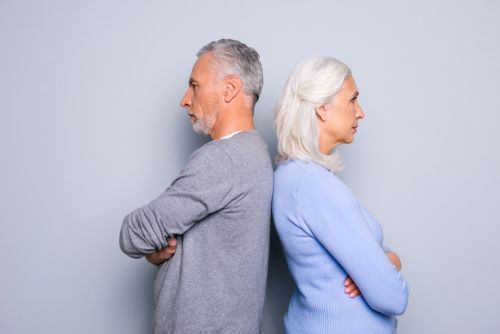 Concept of a gray divorce between a couple over 50. They are standing back to back, with their arms folded in a defensive posture.