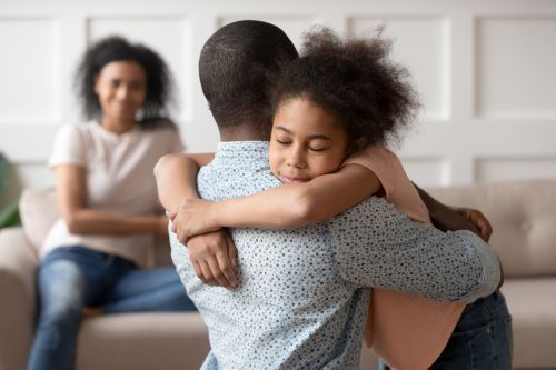How to Help Children Navigate Divorce, divorcing family father reassuring daughter mother supporting them both in the background.