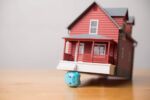 Little piggy bank crushed by large luxury house. Visual concept for a blog disucssing rising bankruptcy rates in CT due to economic pressure.